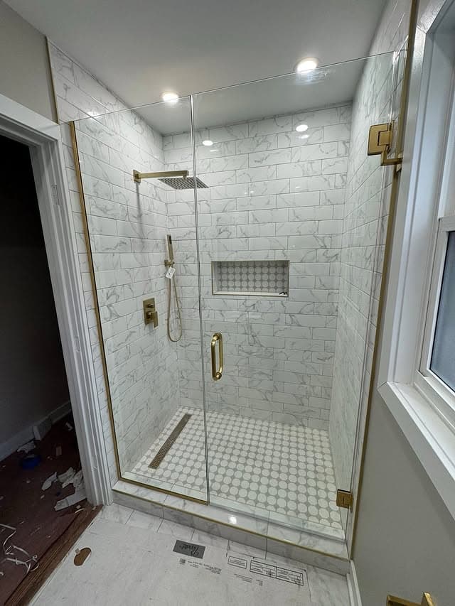 White marble-look shower with brass fixtures, with floor protection still in place